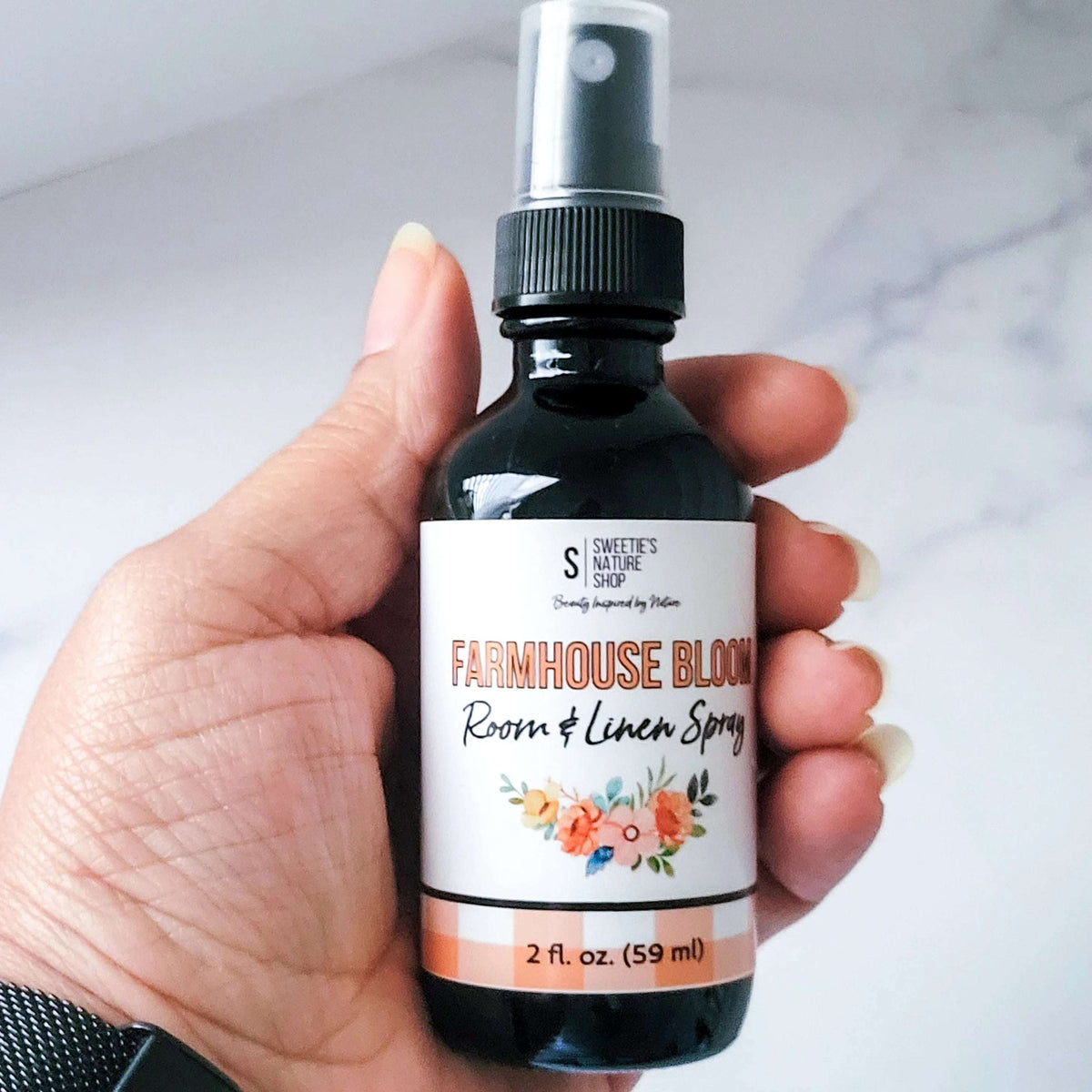 Hand holding a bottle of 'Farmhouse Bloom' room and linen spray with a floral label.