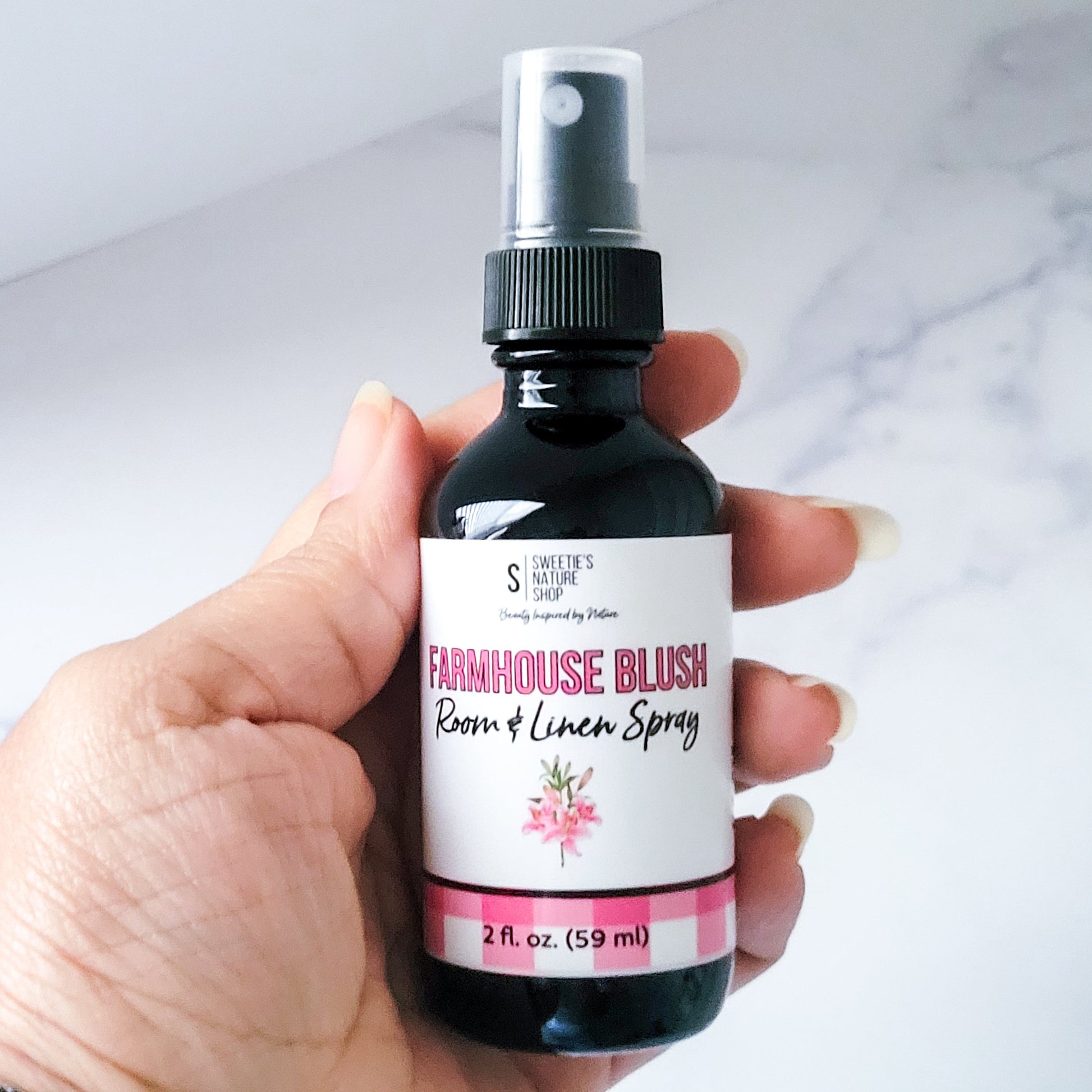 Hand holding a bottle of 'Farmhouse Blush' room and linen spray with a white background