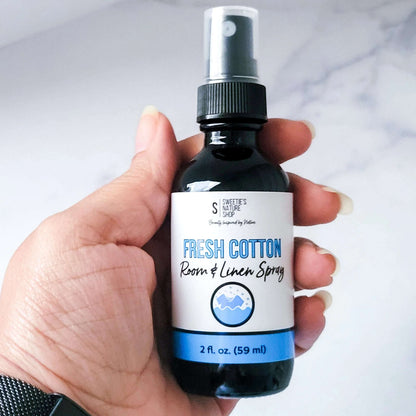 Hand holding a bottle of 'Fresh Cotton' room and linen spray with a white background