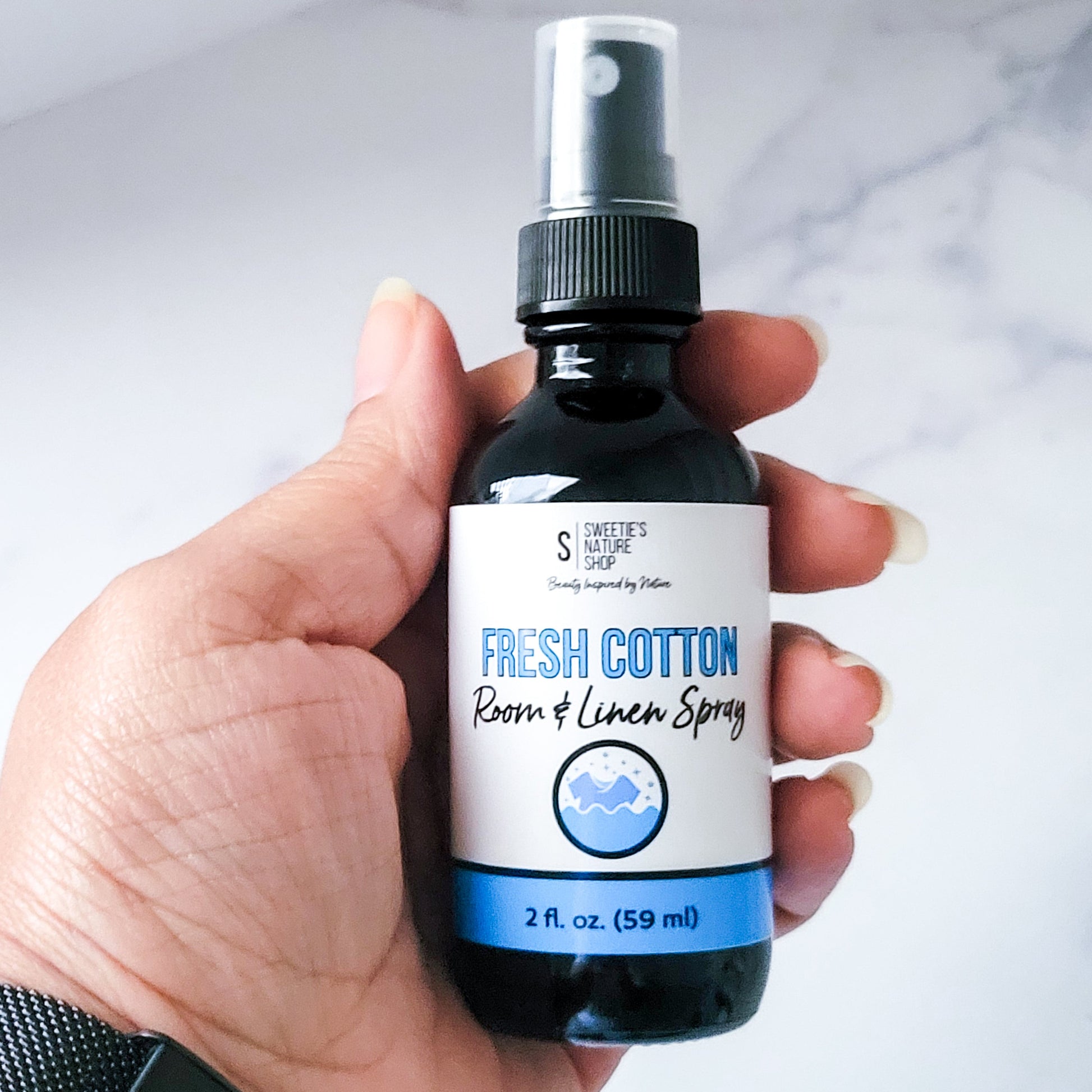 Hand holding a bottle of 'Fresh Cotton' room and linen spray with a white background