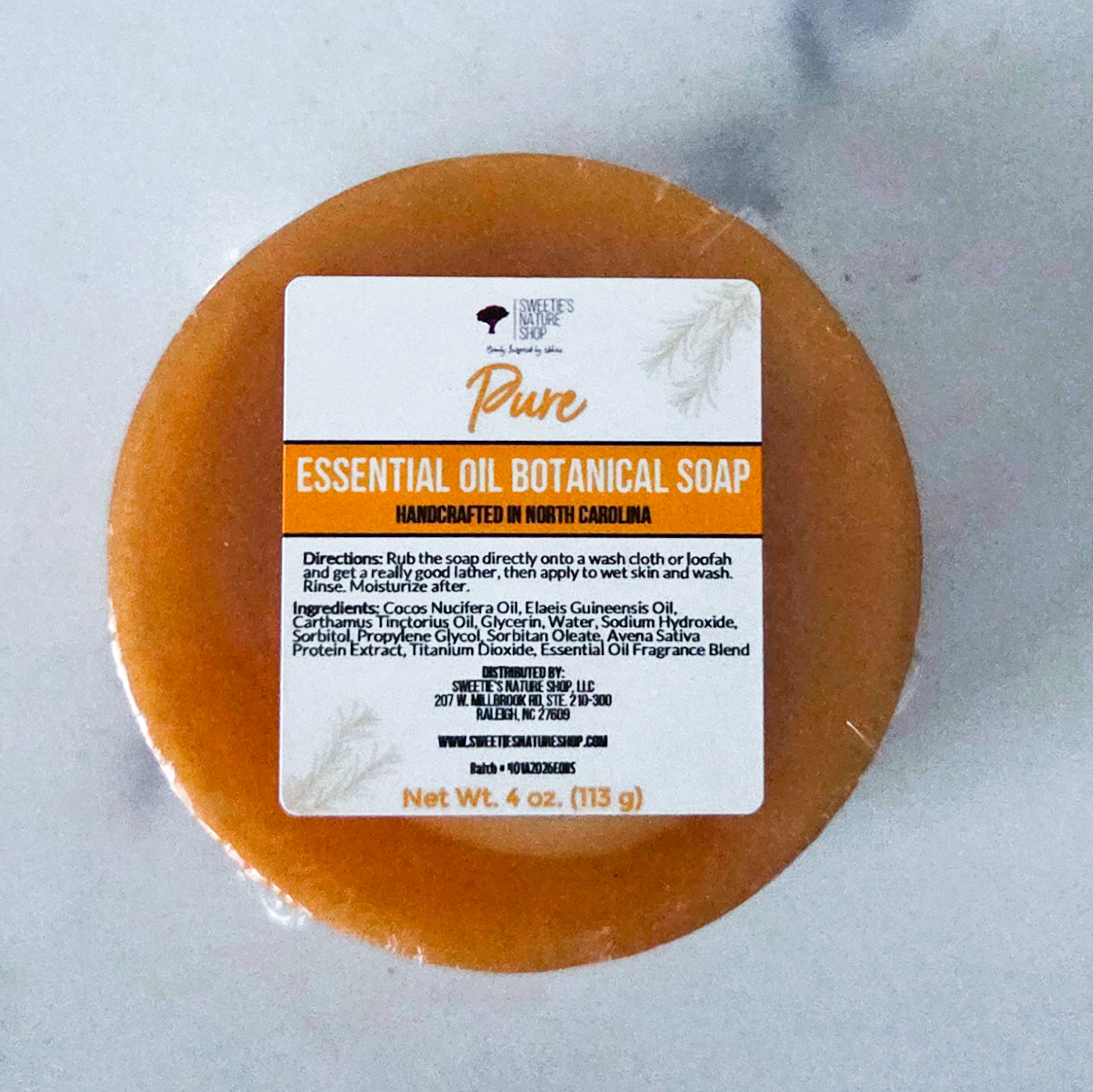 Round soap bar in an orange-gold color — Pure Essential Oil Botanical Soap by Sweetie's Nature Shop, made with orange, lavender, ylang ylang, and rosemary essential oils.